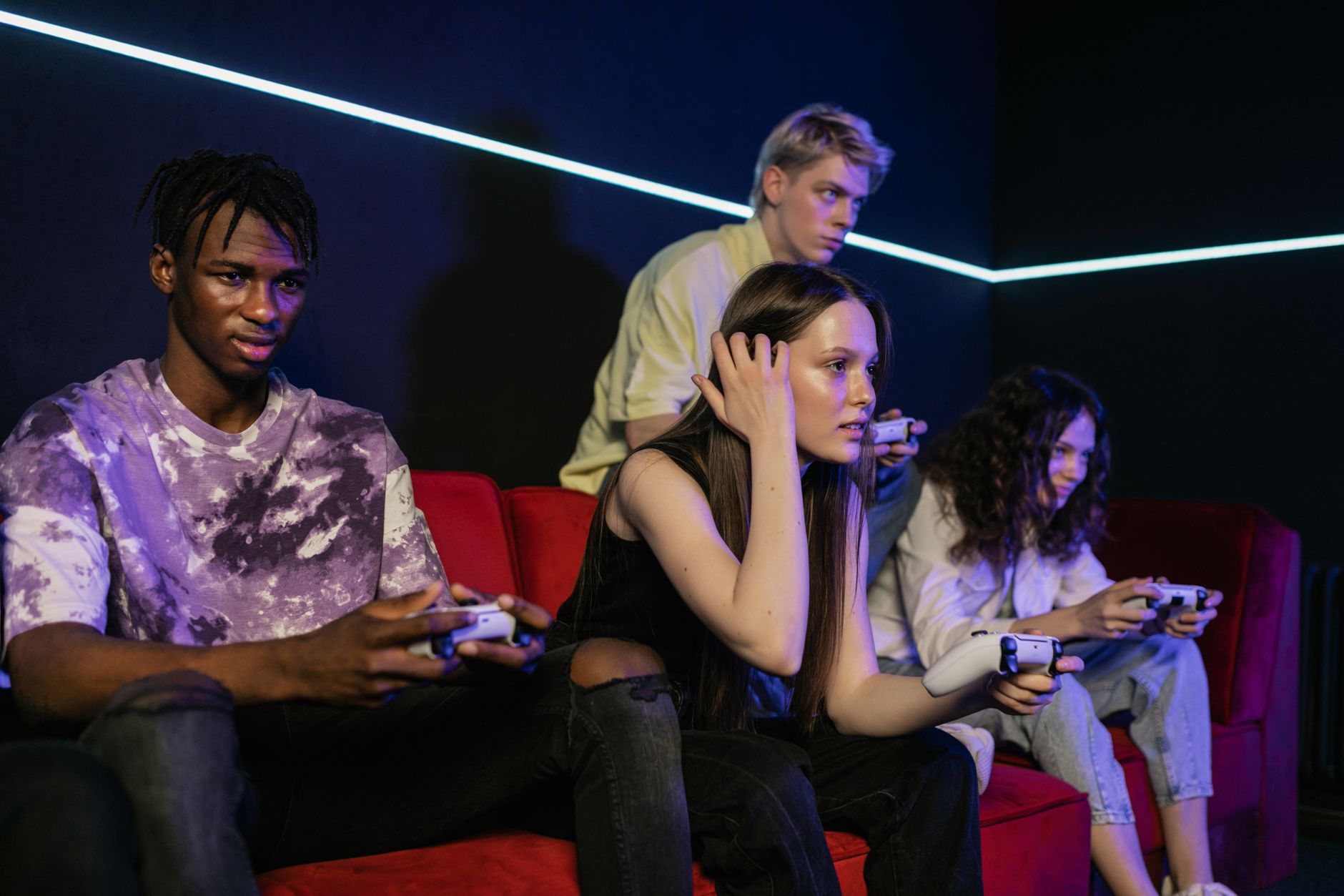 Group of friends enjoying a gaming session on a red sofa with wireless controllers. — Zalety i wady: BLIK online w kasynie ko